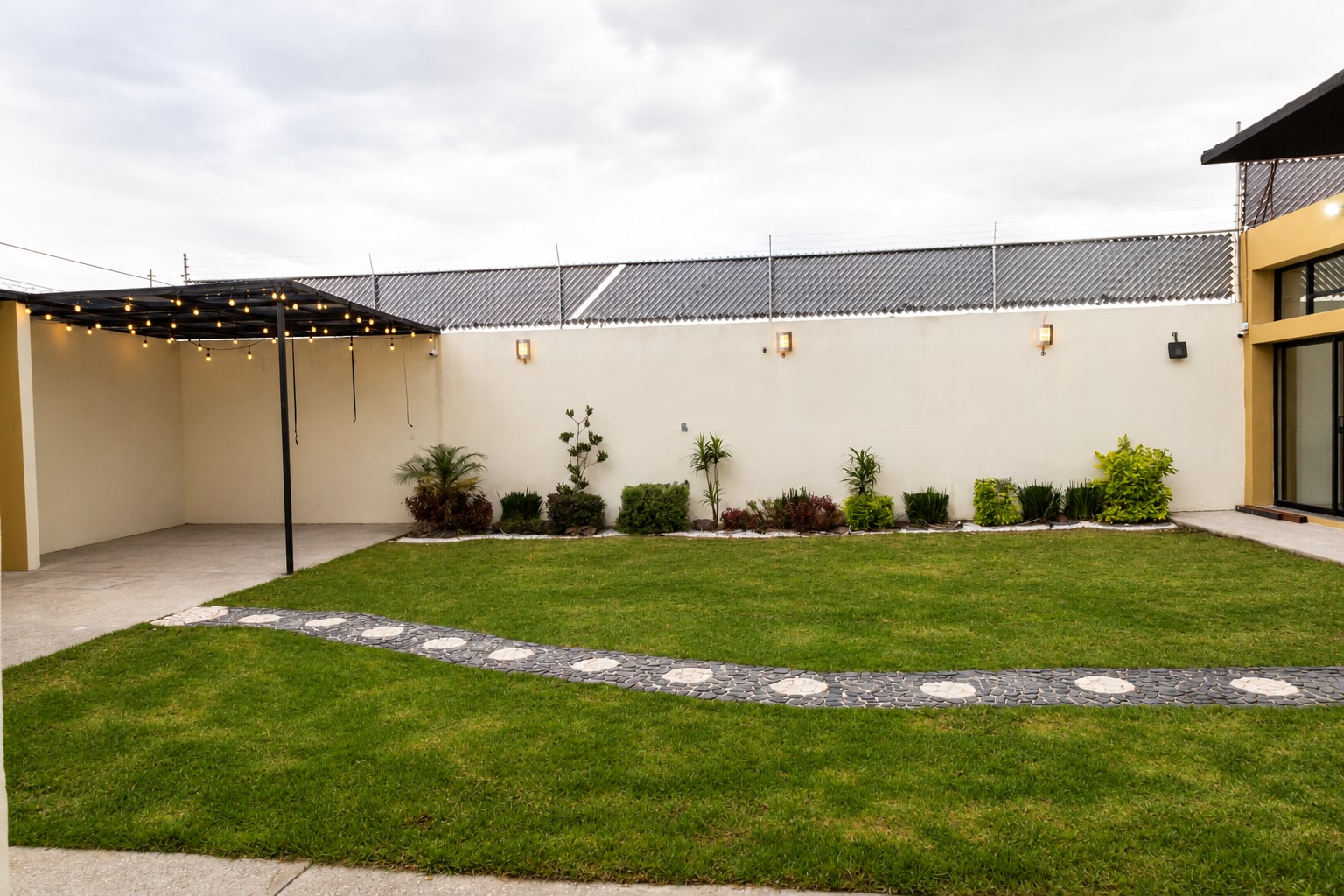 Jardín de Yalduna con sendero de piedra, plantas y pérgola